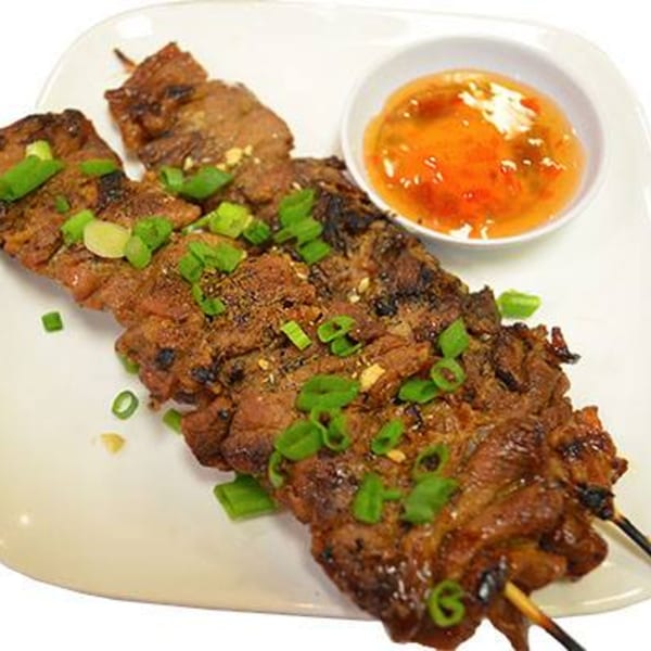 Grilled meat skewers topped with green onions and a side of sweet chili sauce.