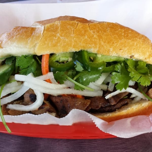 Close-up of a Yummy Deli sandwich with meat, onions, cilantro, and jalapeños in a red basket.