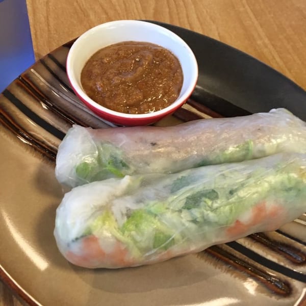 Two fresh spring rolls with shrimp and vegetables, served with a side of peanut dipping sauce.