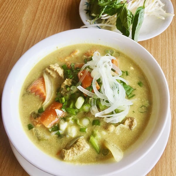 A bowl of Yummy Deli's green curry soup with chicken, tomatoes, onions, and herbs.