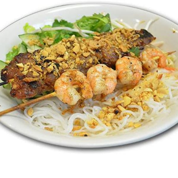 Grilled meat and shrimp skewers with rice noodles, lettuce, and crushed peanuts in a white bowl.