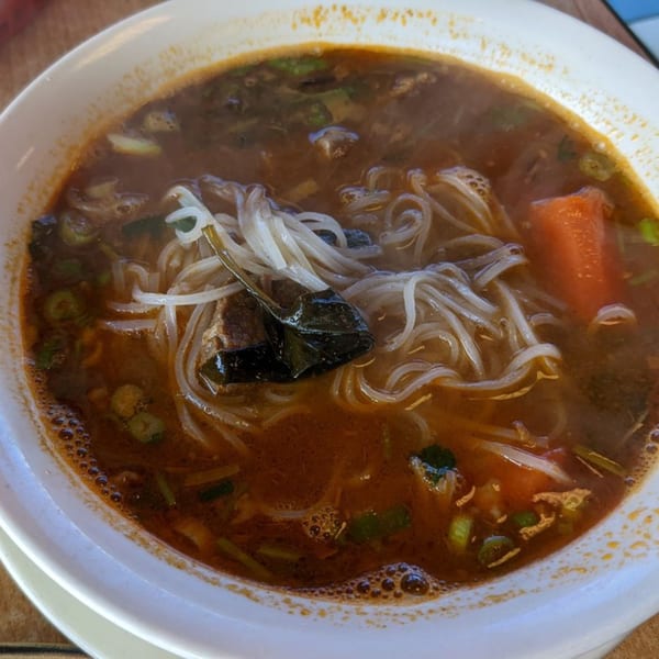 Close-up of a bowl of Yummy Deli's savory noodle soup with meat, vegetables, and broth.