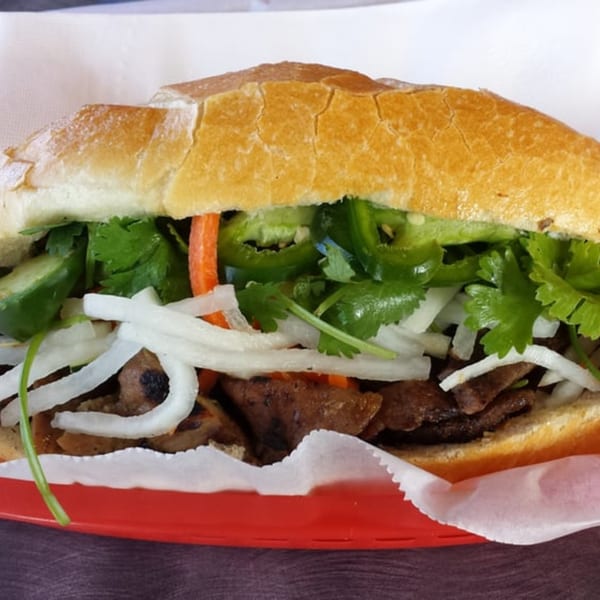 A Yummy Deli sandwich filled with meat, onions, cilantro, and peppers on a red plate.