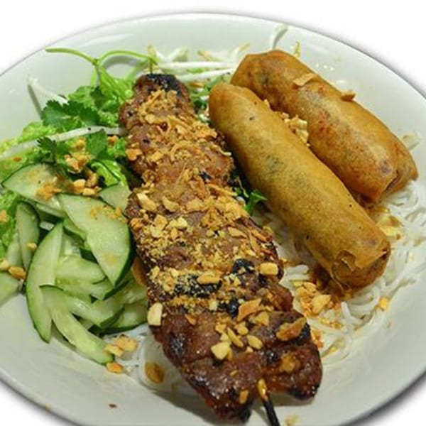 Grilled meat skewer with peanuts, two fried spring rolls, rice noodles, and a side salad.